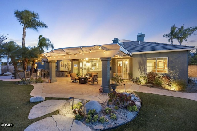 back house at dusk featuring an outdoor fire pit, a lawn, and a patio