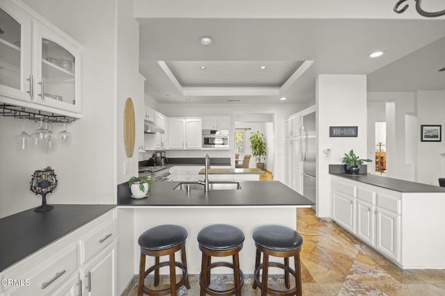 kitchen featuring kitchen peninsula, white cabinets, a raised ceiling, and a breakfast bar area