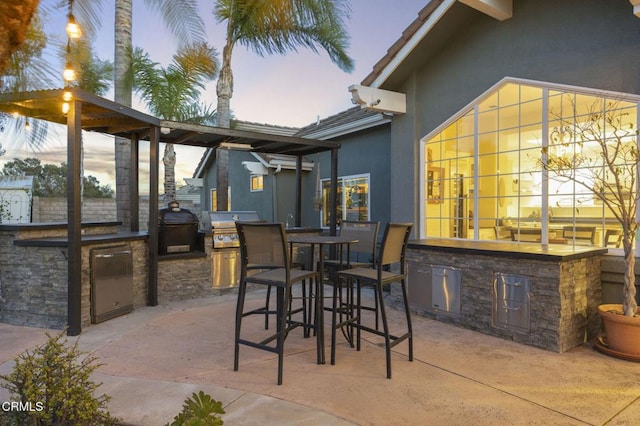 patio terrace at dusk featuring an outdoor bar, exterior kitchen, and area for grilling