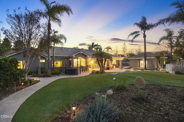 back house at dusk featuring a lawn and a patio