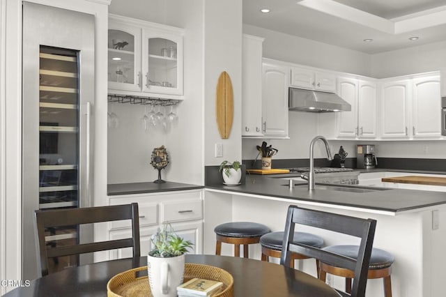 kitchen with a kitchen bar, white cabinetry, sink, a raised ceiling, and kitchen peninsula