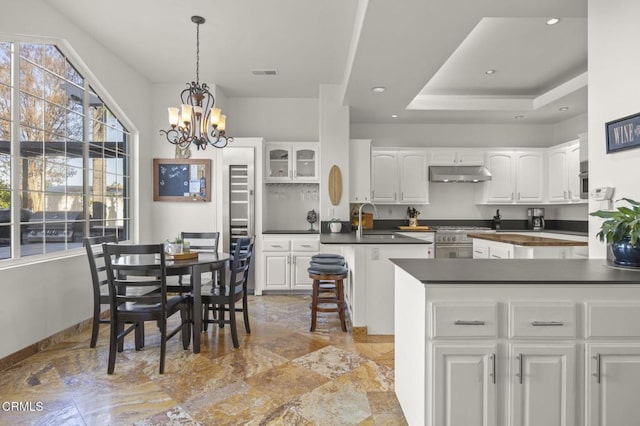 kitchen featuring a raised ceiling, decorative light fixtures, sink, white cabinetry, and stainless steel range