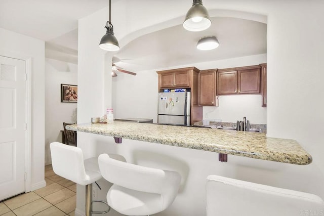 kitchen featuring a peninsula, a kitchen breakfast bar, freestanding refrigerator, brown cabinets, and pendant lighting