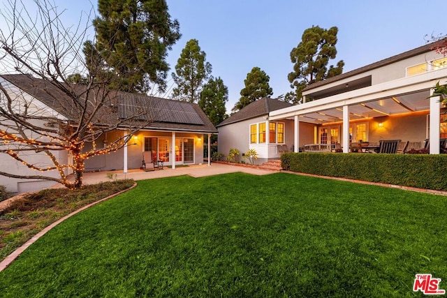 back of property with a patio area, a lawn, and solar panels