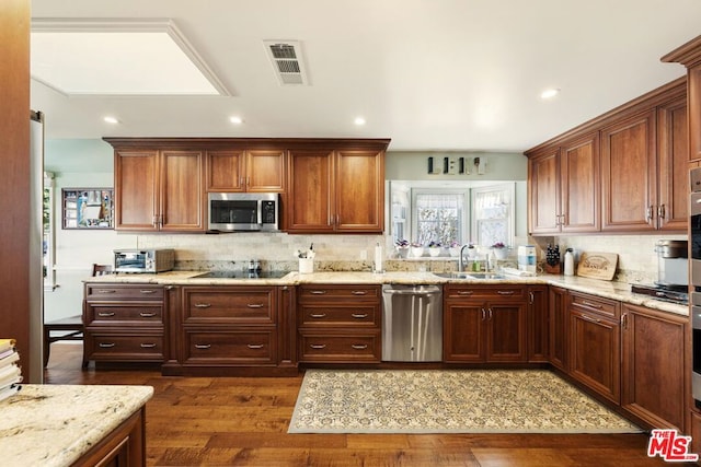 kitchen with light stone countertops, dark hardwood / wood-style flooring, stainless steel appliances, decorative backsplash, and sink