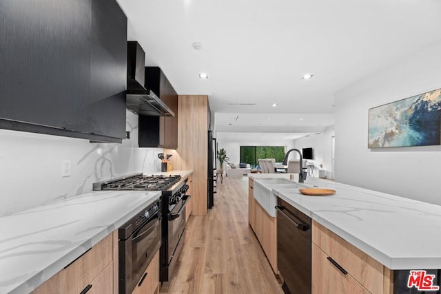 kitchen featuring tasteful backsplash, wall chimney range hood, black appliances, light stone counters, and sink