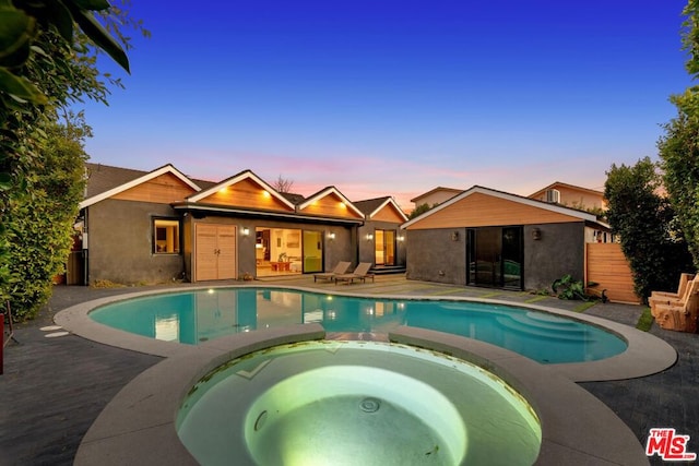 pool at dusk with an in ground hot tub