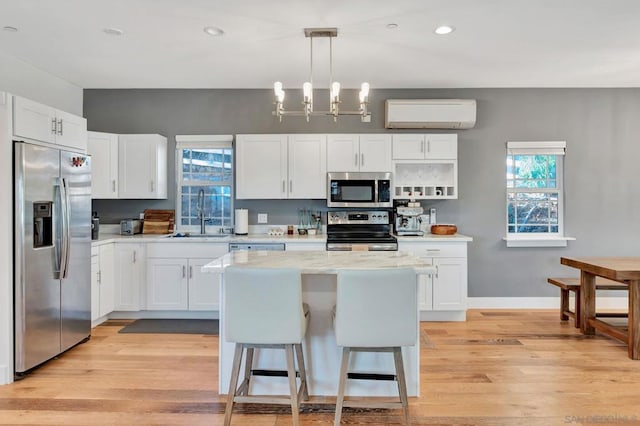 kitchen featuring appliances with stainless steel finishes, a wall mounted air conditioner, white cabinetry, sink, and pendant lighting