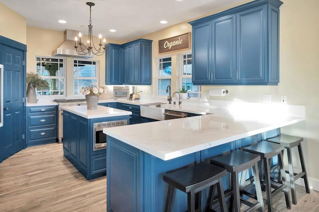 kitchen with a center island, blue cabinetry, light hardwood / wood-style floors, appliances with stainless steel finishes, and ventilation hood