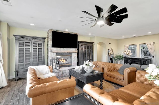 living room featuring ceiling fan, a stone fireplace, and light hardwood / wood-style floors