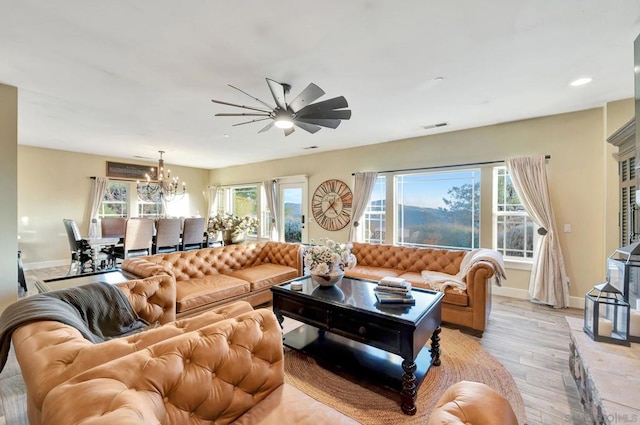 living room with ceiling fan with notable chandelier, light wood-type flooring, and a healthy amount of sunlight