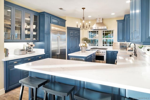 kitchen with premium appliances, wall chimney range hood, and blue cabinetry