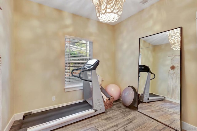 exercise area with wood-type flooring and an inviting chandelier