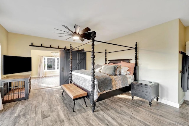 bedroom with light hardwood / wood-style flooring, ceiling fan, and a barn door