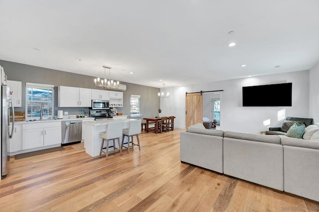 living room with sink, light wood-type flooring, a chandelier, and a barn door