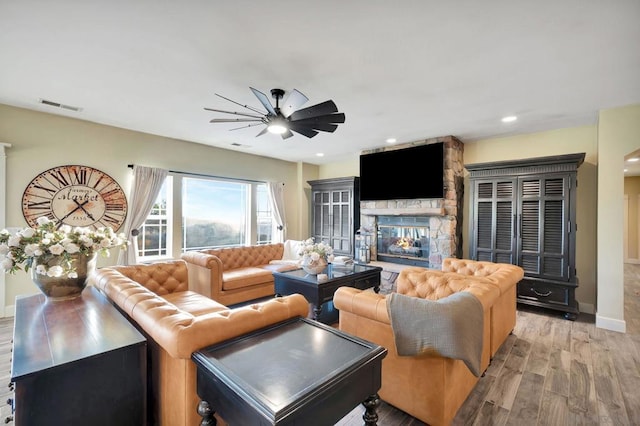 living room with light hardwood / wood-style floors, ceiling fan, and a stone fireplace