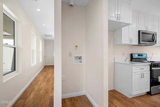 kitchen with light hardwood / wood-style floors, light stone counters, white cabinets, and stainless steel appliances