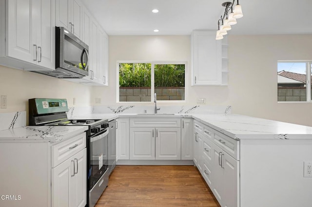 kitchen with appliances with stainless steel finishes, white cabinetry, sink, hanging light fixtures, and kitchen peninsula