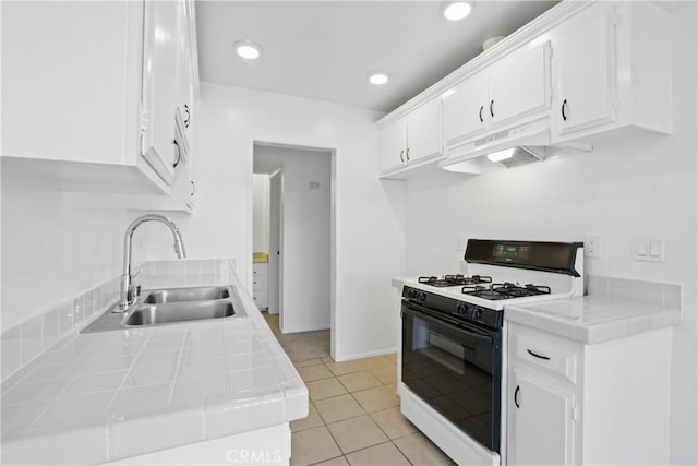 kitchen with sink, light tile patterned floors, white cabinetry, tile counters, and gas range oven