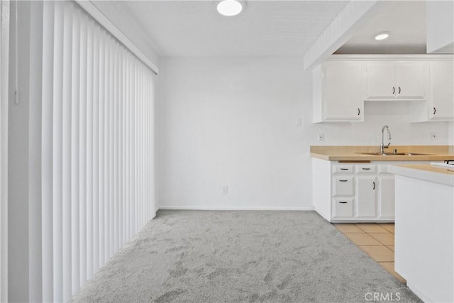 kitchen with light colored carpet, sink, and white cabinets