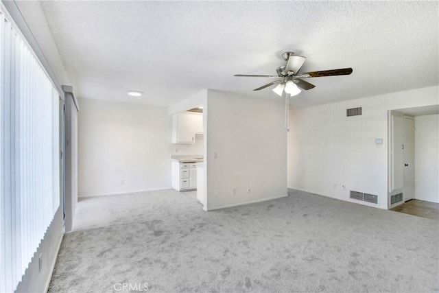 unfurnished living room featuring a textured ceiling, light colored carpet, and ceiling fan