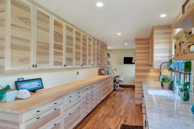 kitchen with butcher block counters, light brown cabinetry, built in desk, and light hardwood / wood-style flooring