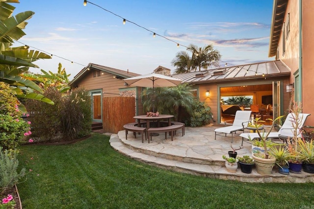 back house at dusk featuring a yard and a patio area