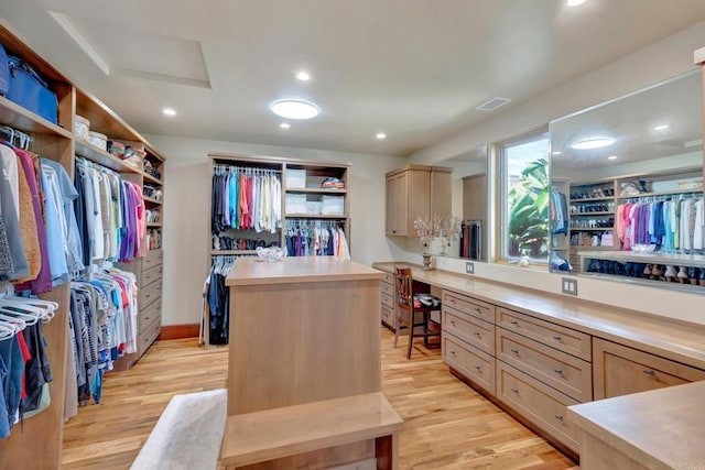 spacious closet with built in desk and light hardwood / wood-style floors