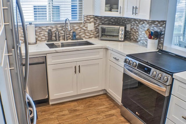 kitchen featuring hardwood / wood-style floors, sink, white cabinets, light stone counters, and stainless steel appliances