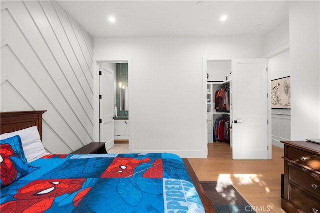 bedroom with connected bathroom, a spacious closet, a closet, and light wood-type flooring