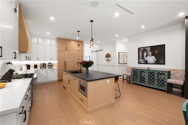 kitchen featuring appliances with stainless steel finishes, sink, white cabinets, a barn door, and a center island with sink