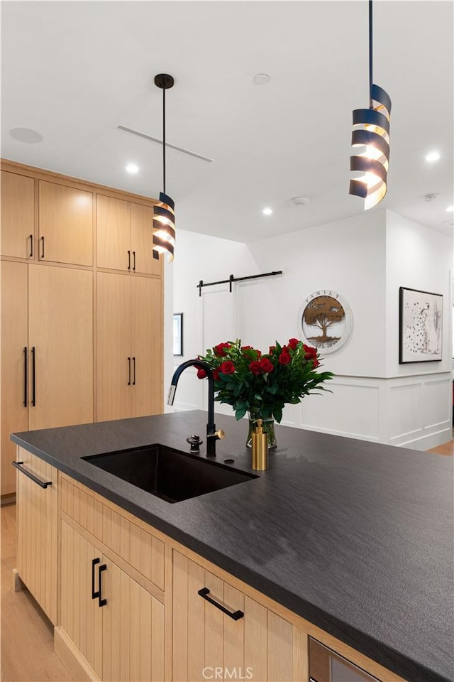 kitchen featuring decorative light fixtures, sink, a barn door, light brown cabinets, and light wood-type flooring