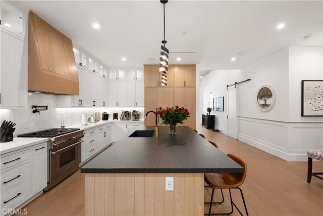 kitchen with white cabinetry, high end range, a kitchen island with sink, custom exhaust hood, and a barn door