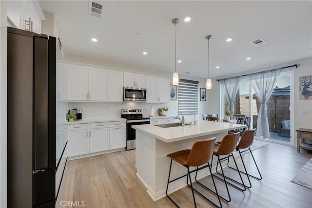 kitchen featuring white cabinetry, appliances with stainless steel finishes, hanging light fixtures, and a center island with sink