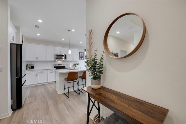 kitchen featuring pendant lighting, appliances with stainless steel finishes, white cabinetry, a kitchen island with sink, and tasteful backsplash