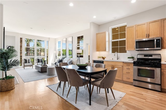 kitchen with appliances with stainless steel finishes, tasteful backsplash, light brown cabinetry, sink, and light hardwood / wood-style flooring