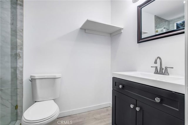 bathroom with toilet, a tile shower, and vanity