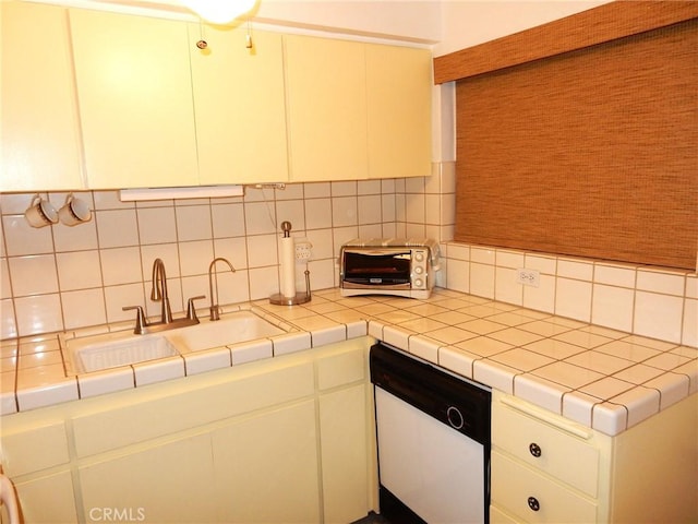 kitchen featuring tasteful backsplash, dishwasher, sink, white cabinets, and tile counters