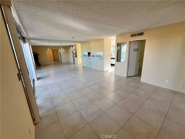 empty room featuring an inviting chandelier, a textured ceiling, and light tile patterned floors