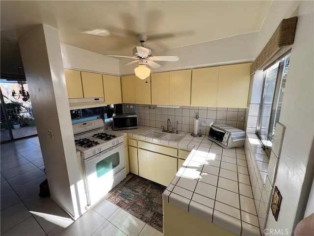 kitchen featuring sink, ceiling fan, decorative backsplash, tile countertops, and white gas stove