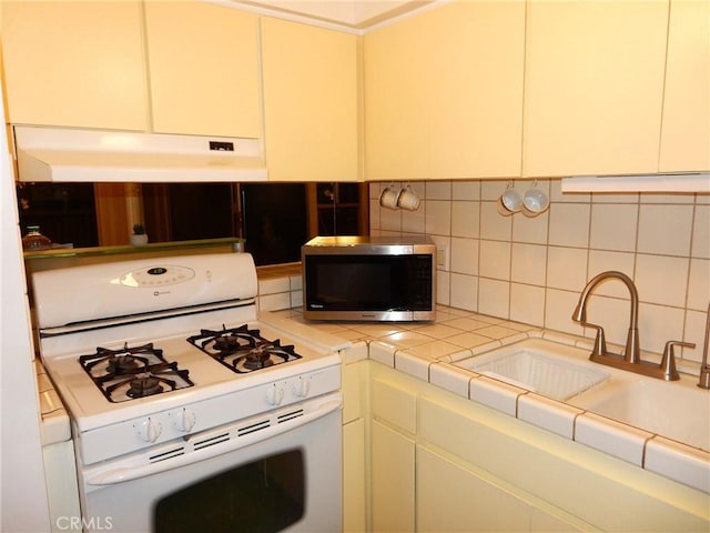 kitchen with tasteful backsplash, white gas range, sink, and tile countertops