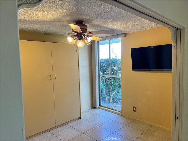 unfurnished bedroom featuring ceiling fan, light tile patterned floors, a textured ceiling, and a closet