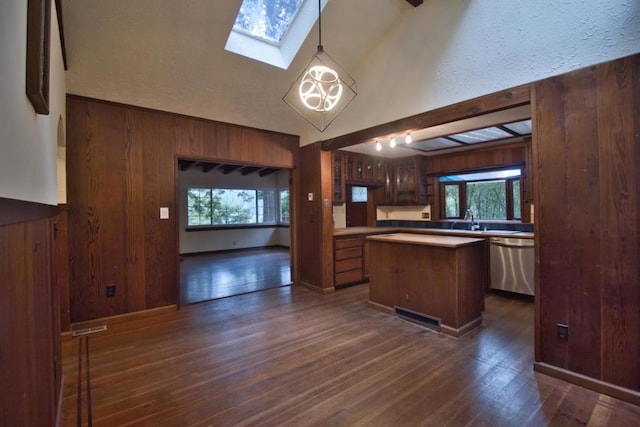 kitchen with decorative light fixtures, stainless steel dishwasher, a center island, and wood walls