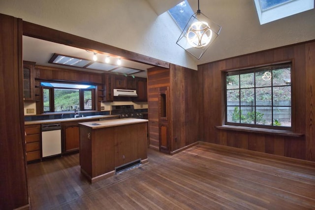 kitchen with vaulted ceiling with skylight, wood walls, a center island, hanging light fixtures, and gas range