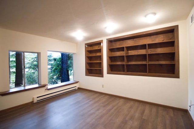 spare room featuring built in shelves, a baseboard heating unit, and dark wood-type flooring