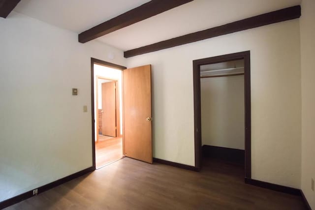 unfurnished bedroom featuring beam ceiling, a closet, and dark hardwood / wood-style flooring