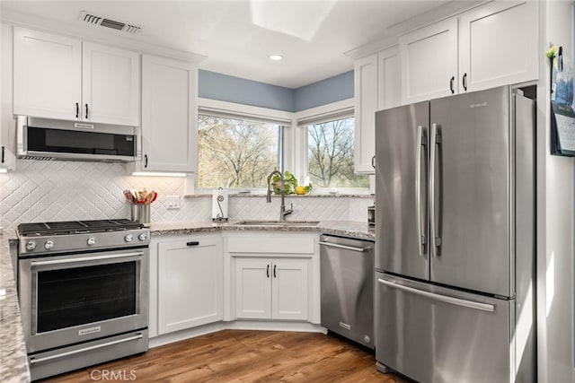 kitchen with dark hardwood / wood-style flooring, sink, appliances with stainless steel finishes, white cabinets, and light stone counters