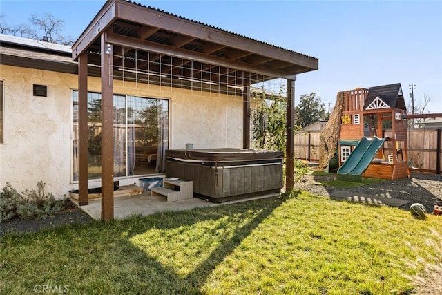 rear view of property with a playground, a patio area, a yard, and a hot tub