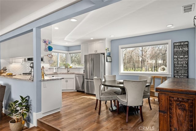 kitchen featuring white cabinets, stainless steel appliances, tasteful backsplash, light hardwood / wood-style floors, and light stone counters