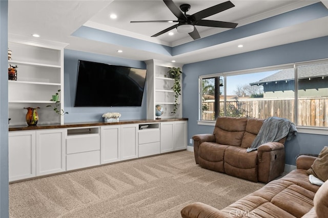 living room featuring ceiling fan, light carpet, built in features, and a raised ceiling